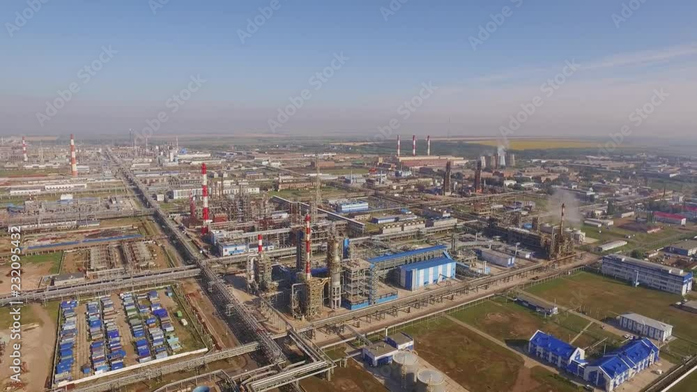 Giant oil refinery in rural areas on a summer sunny day with a clear blue sky. Red and white pipes, a huge territory among agricultural crops - Aerial view. Giant oil refinery in rural areas on a summer sunny day with a clear blue sky. Red and white pipes, a huge territory among agricultural crops - Aerial view.