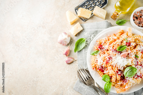 Italian food, fusilli pasta with  tomato sauce, grated parmesan cheese and basil, light stone table copy space top view