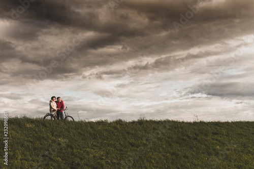 Senior couple with bicycles in rural landscape under cloudy sky