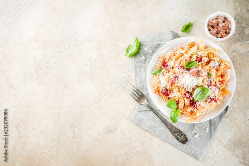 Italian food, fusilli pasta with tomato sauce, grated parmesan cheese and basil, light stone table copy space top view