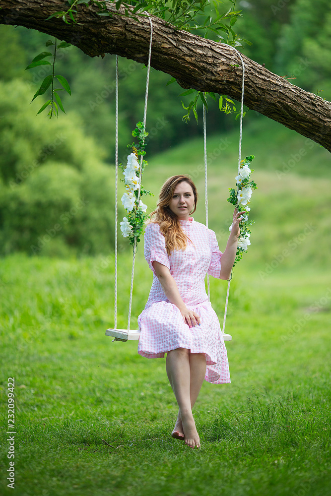 Beautiful girl in summer dress rides on the swing.