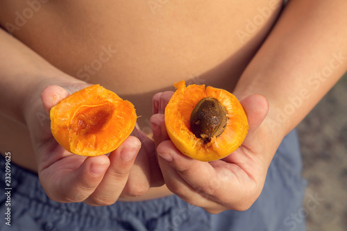 the boy holds the halves of apricots
