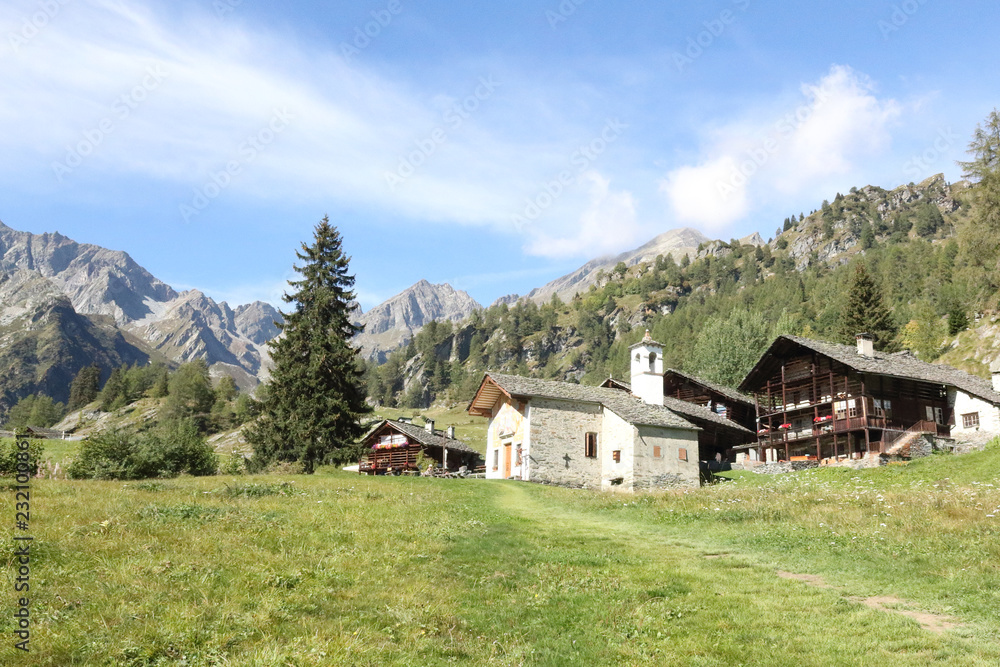 The Walser town of Follu, with wood and stone lodges, high mountains, forests and pastures, in summer, in Val d'Otro valley, Alps mountains, Italy