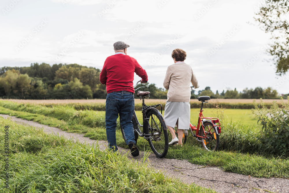 Senior couple pushing bicycles in rural landscape Senior couple pushing bicycles in rural landscape