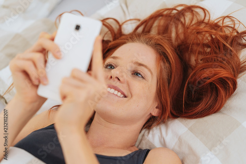 Young smiling woman using mobile phone in bed
