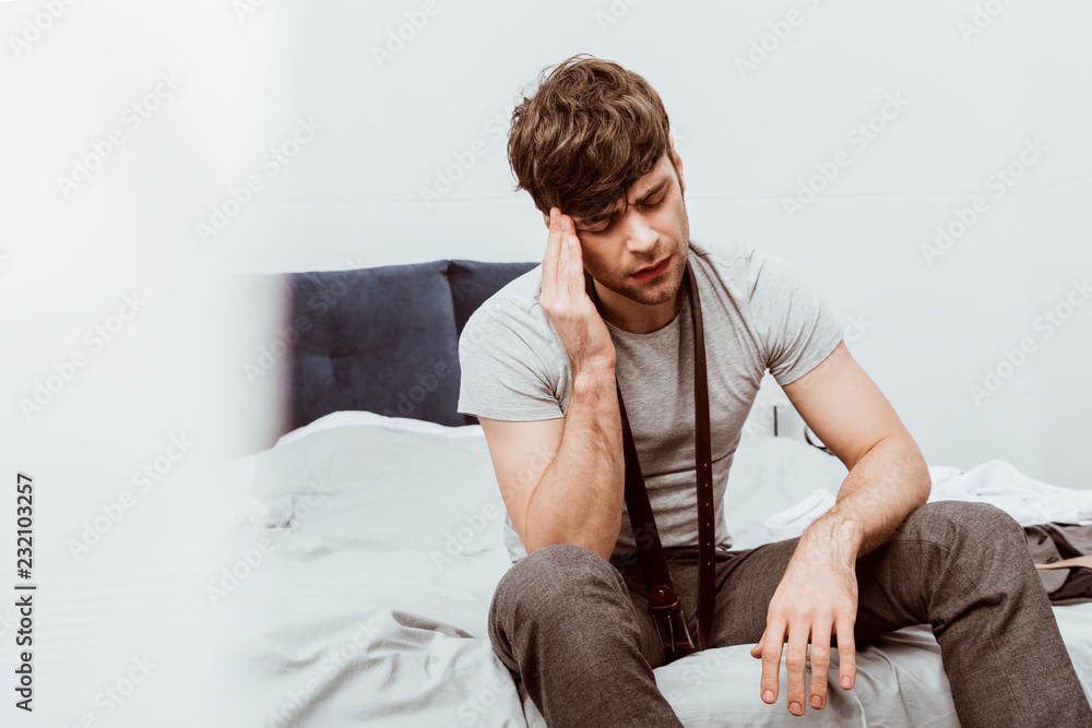 handsome young businessman with belt over neck sitting on bed and having headache at home handsome young businessman with belt over neck sitting on bed and having headache at home