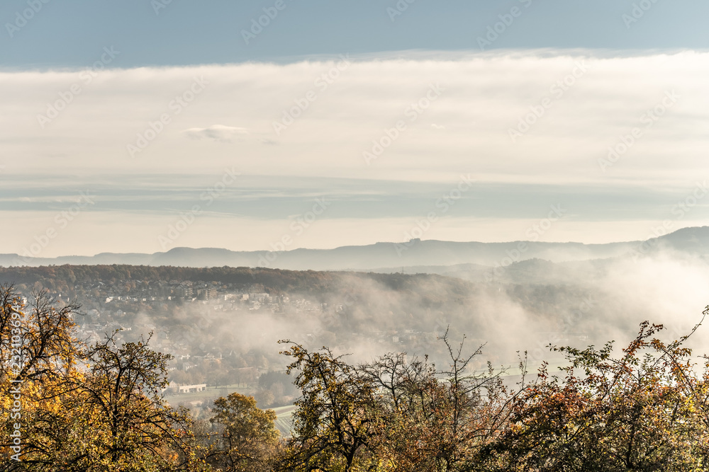 Herbstliche Baumgruppe mit sich auflösendem Nebel und Wolken vor Albpanorama