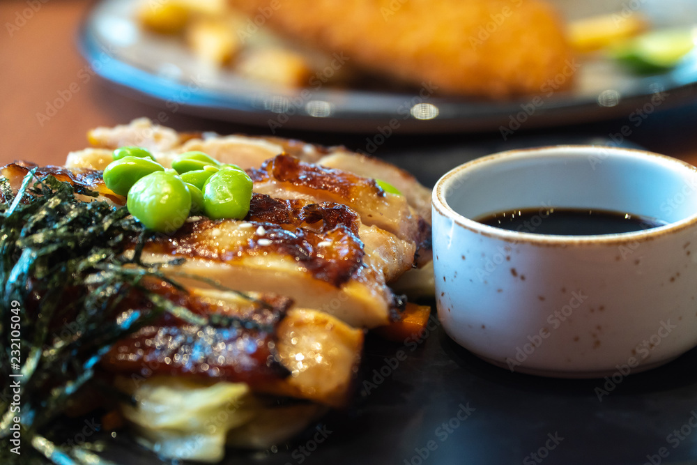 close up of chicken steaks with cup of sauce on the black plate. Green peas and Japanese seaweed on chicken steaks with white cabbage, carrots and mushrooms in the restaurant close up of chicken steaks with cup of sauce on the black plate. Green peas and Japanese seaweed on chicken steaks with white cabbage, carrots and mushrooms in the restaurant