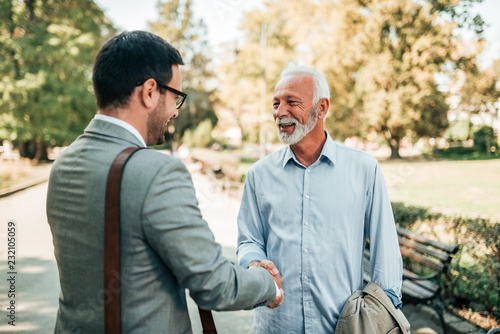 Portrait of a senior and young men handshaking in the park. © bnenin