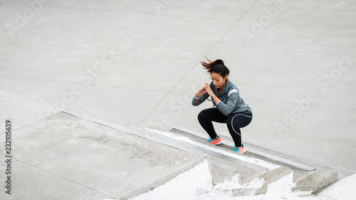 Latin urban sporty woman training. Female athlete doing squat jumps on urban stairs.