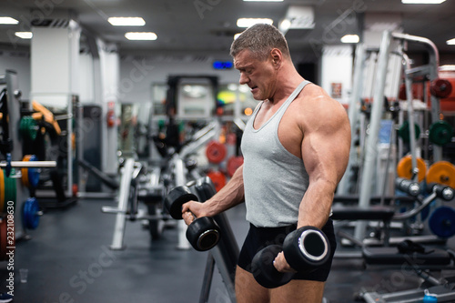 Fototapeta Naklejka Na Ścianę i Meble -  athletic man trains in the gym. Training biceps with a dumbbells