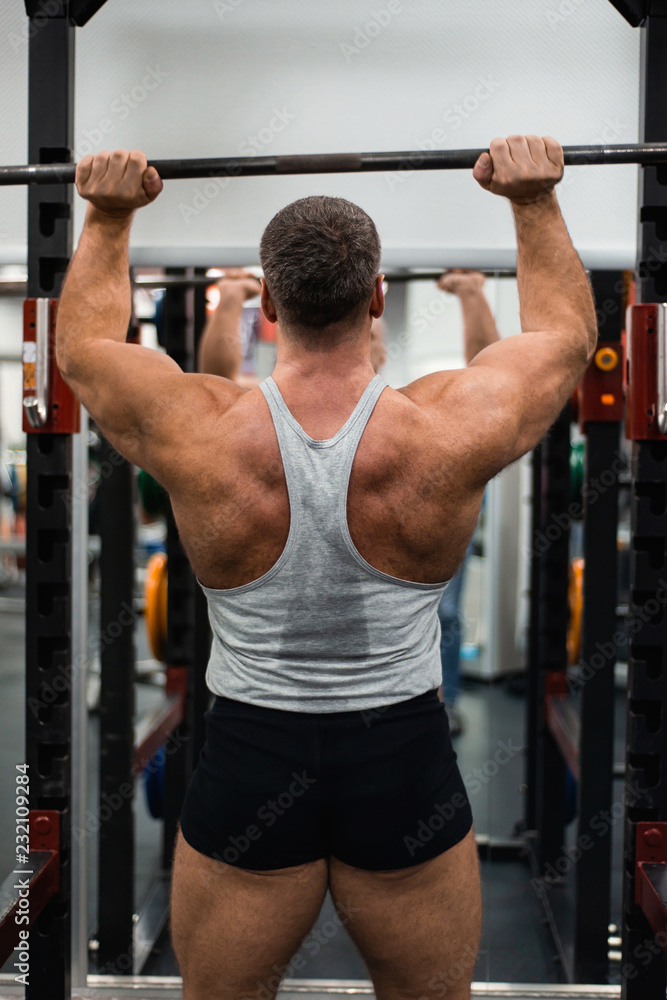 Naklejka premium muscular man trains his shoulders with a barbell in the gym. Health and fitness concept