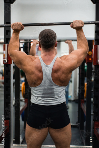 muscular man trains his shoulders with a barbell in the gym. Health and fitness concept