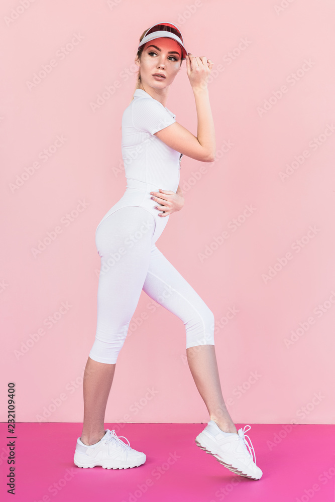 sportswoman in visor hat looking away and posing on pink