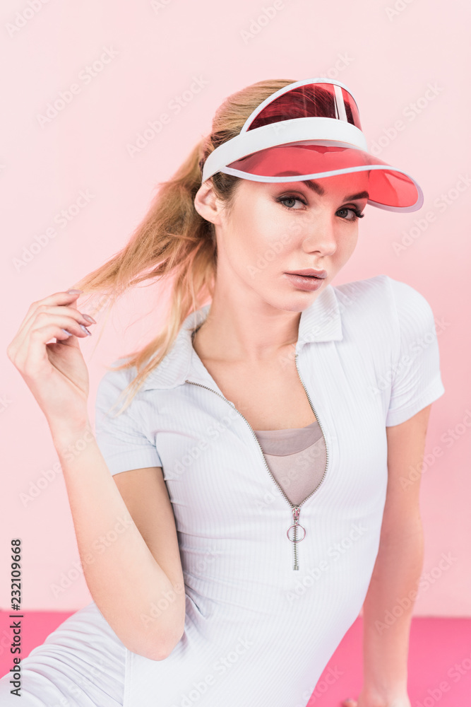 portrait of beautiful sportswoman in visor hat looking at camera on pink portrait of beautiful sportswoman in visor hat looking at camera on pink