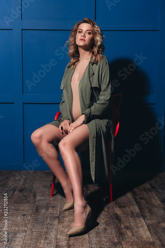 Beautiful pregnant woman, model with a curly hair, blue background, pregnant in a trench coat