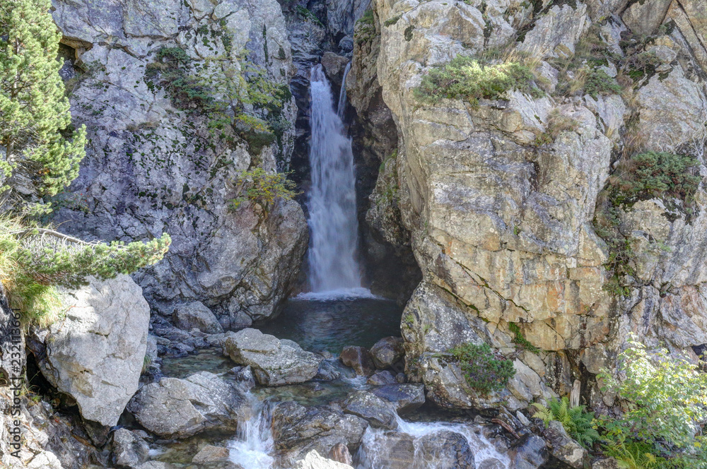 A Caldarès river waterfall during a sunny autumn in the firs and pine trees forest of the rocky mountains of Panticosa, Aragon Pyrenees, Spain