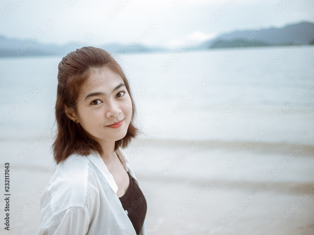Asian girl looking over shoulder while standing on tropical beach. Portrait of happy young woman smiling at sea. sweet smile. Vintage Tone. copy space... Asian girl looking over shoulder while standing on tropical beach. Portrait of happy young woman smiling at sea. sweet smile. Vintage Tone. copy space...