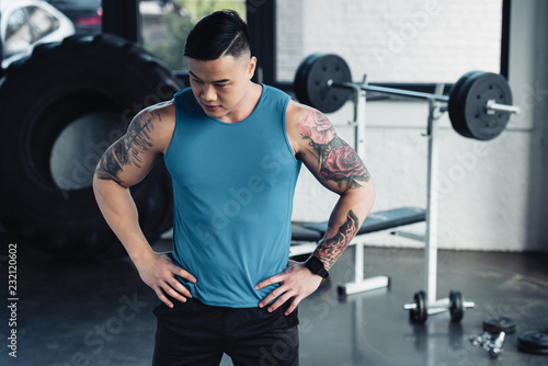 young asian sportsman with hands on hips at gym