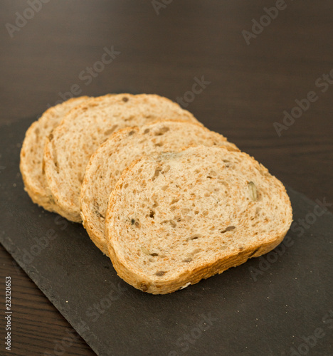 Slices of homemade multigrain bread on black slate board