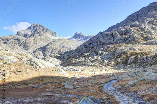 A path going through high rocky barren mountains with yellow grass and a blue sky in a sunny autumn, in Panticosa, Aragon Pyrenees, Spain