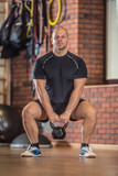 Strong muscular man exercising with kettlebell facilities in gym or workout center