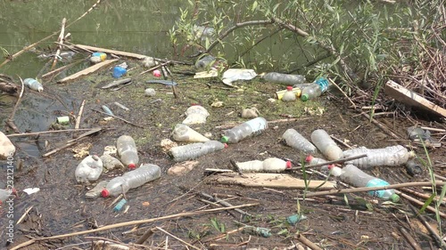 Plastic pollution: bottles left by campers thrown as garbage to a muddy river.
