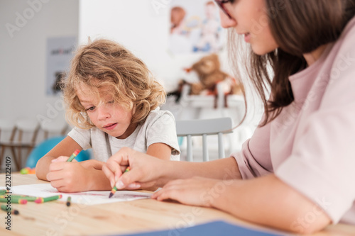 Bild auf Leinwand Close-up of a child with an autism spectrum disorder and the therapist by a table drawing with crayons during a sensory integration session