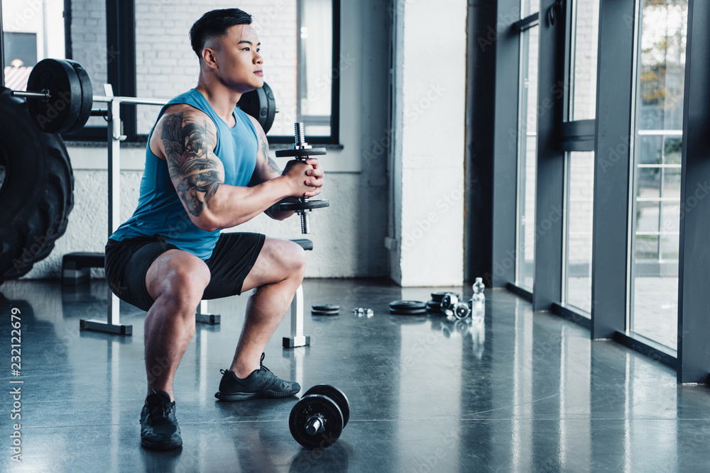 concentrated young sportsman exercising with dumbbells in gym concentrated young sportsman exercising with dumbbells in gym