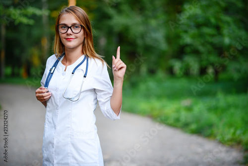 Worth knowing. young girl who is a doctor stands outside, raised the index finger of his left hand up