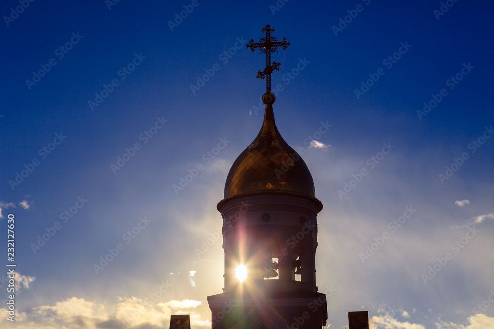 Old Christian church in Kemerovo with golden and gilded domes, brown granite walls against a sky and sunset. Concept of faith in god, orthodoxy, prayer