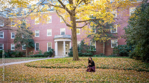Thai woman kneeling in front of university building in the fall