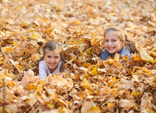 Children are lying and playing on fallen leaves in autumn city park.