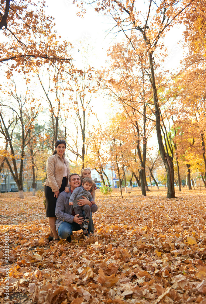 Parents and child are posing in autumn city park. Bright yellow trees.