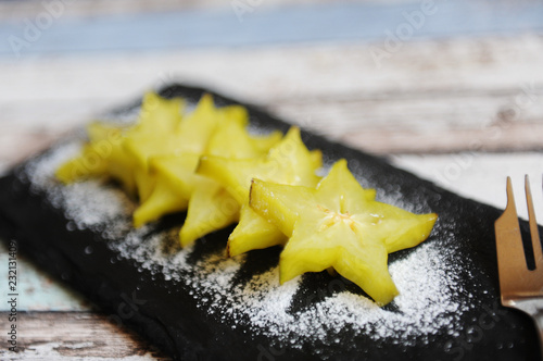 Carambola pieces served with icing sugar on a black slate plate