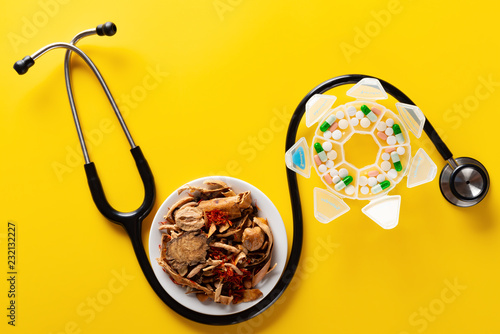 studio shoot Chinese herb medicine and pills wrapped with a stethoscope on yellow background photo