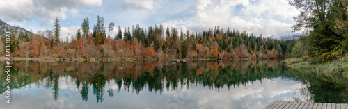 fall color forest and foliage panorama landscape surround an idyllic mountain lake in the Alps of Switzerland on a late autumn day with reflections in the water with a wooden boardwalk in the foregrou