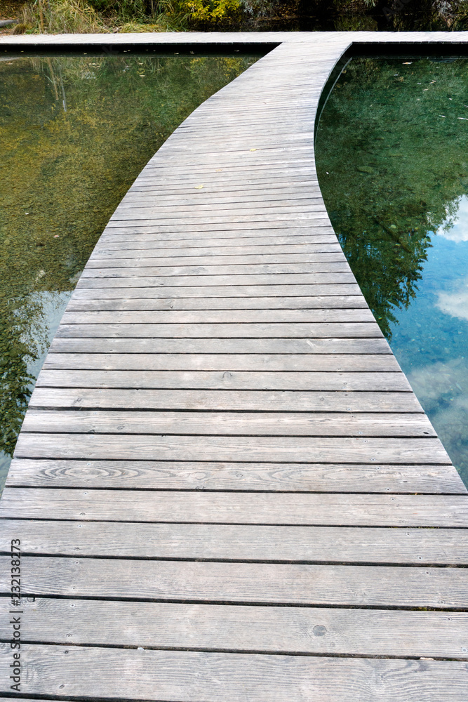 Fototapeta premium long curved wooden boardwalk and footpath over a blue mountain lake with reflections in the water