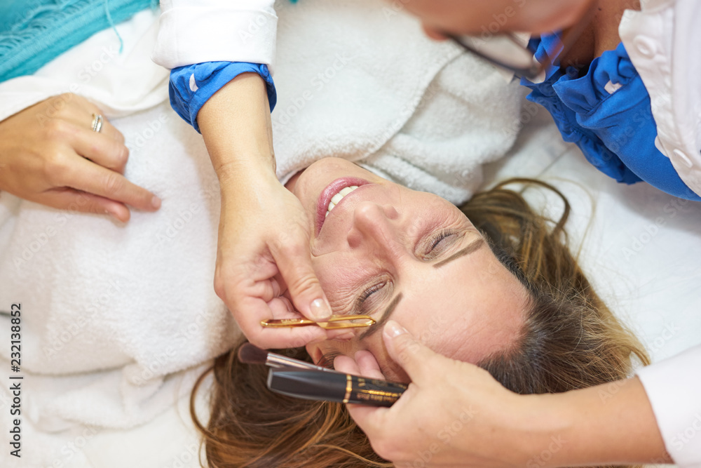 middle-aged woman getting eyebrows plucked middle-aged woman getting eyebrows plucked