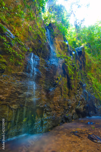 Waterfall on a steep high cliff in the thickets of the rainforest, blue water on the brown stones. Wild jungle on the Lanta island, Krabi, Thailand.