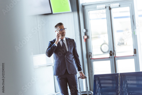 adult handsome businessman with smartphone and baggage walking at airport