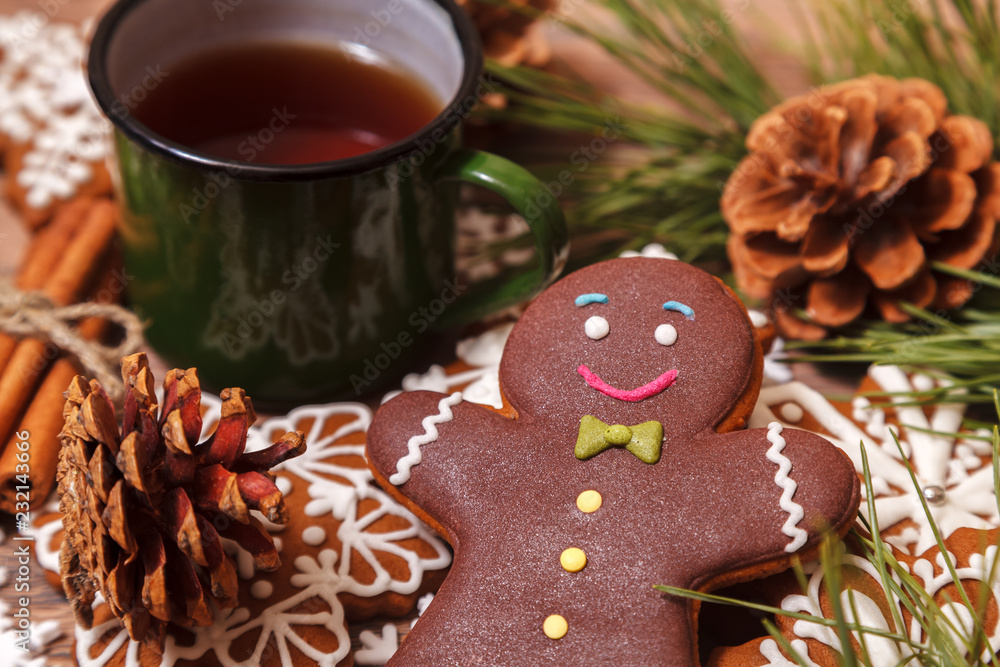 Christmas background. Tea in a metal green mug, traditional Christmas gingerbread, Christmas tree branches and cones on a wooden background close-up, top view Christmas background. Tea in a metal green mug, traditional Christmas gingerbread, Christmas tree branches and cones on a wooden background close-up, top view