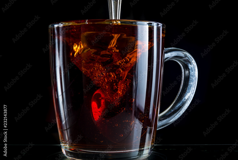Brewing a tea bag in a transparent mug with sugar on a black background, a storm in a glass Brewing a tea bag in a transparent mug with sugar on a black background, a storm in a glass