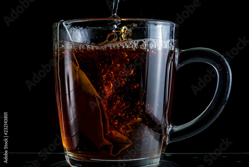 Brewing a tea bag in a transparent mug with sugar on a black background, a storm in a glass