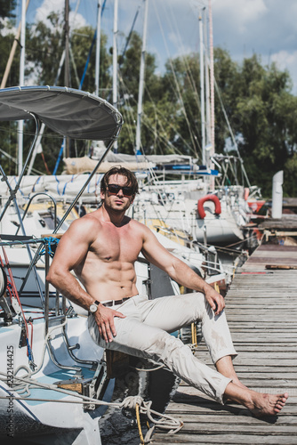 Sexy muscular man near yacht club at warm sunny day. Concept of traveling and adventure. Vintage tones 