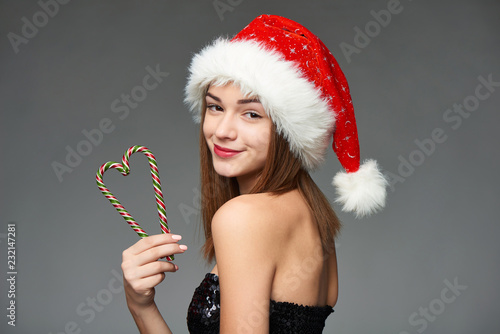 Closeup of beautiful girl in Santa hat holding Christmas candies composed in heart shape