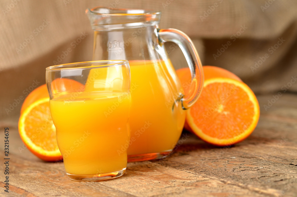 Glass full of orange juice, carafe with fresh juice and fresh oranges in the background on wooden table Glass full of orange juice, carafe with fresh juice and fresh oranges in the background on wooden table