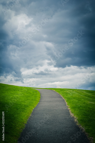 Natural background with a path up the hill, green grass and clouded sky