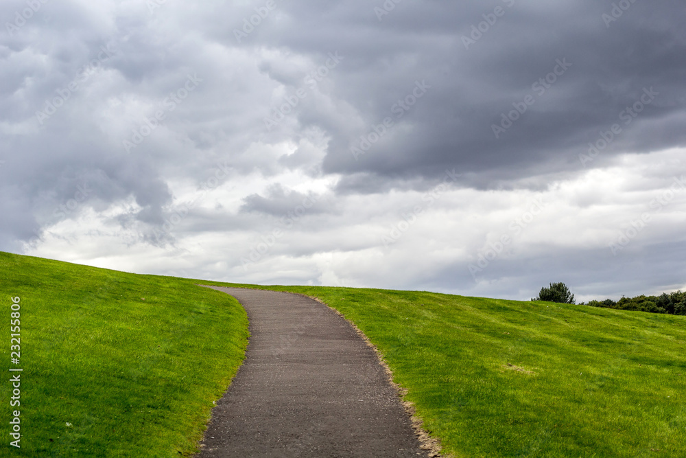 Natural background with a path up the hill, green grass and clouded sky