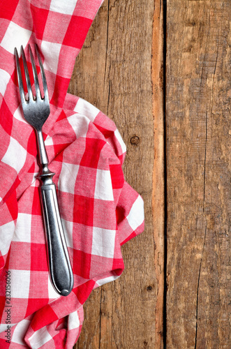 Fork on red checkered tablecloth right frame on vintage wooden table background - view from above - vertical photo
